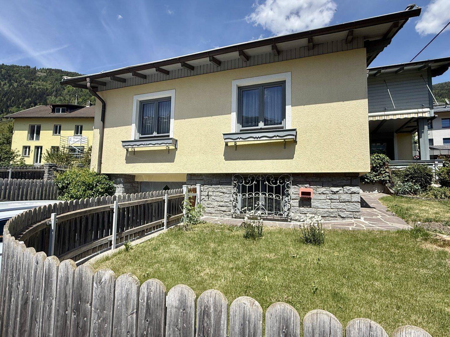 Seitenansicht des Hauses mit gelber Fassade, Steinsockel und kleinem Vorgarten.