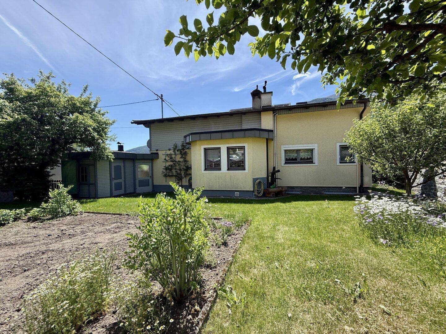 Rückseite des Hauses mit großem Gartenbereich und vorbereitetem Beet für Pflanzen.