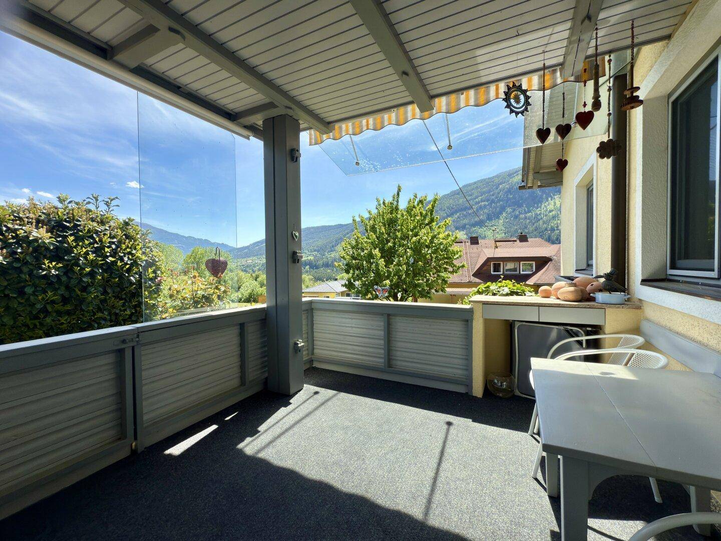 Überdachter Balkon mit Glasbrüstung, Sitzgelegenheiten und weitem Bergblick.