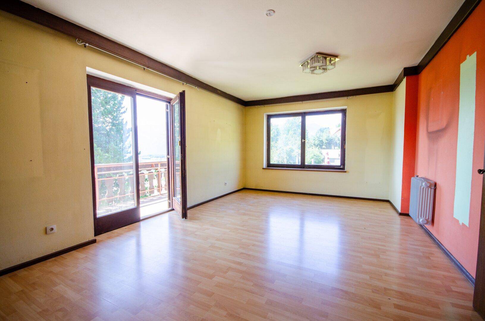 Heller Wohnraum mit Holzboden, farbigen Wänden und direktem Zugang zu einem Balkon.