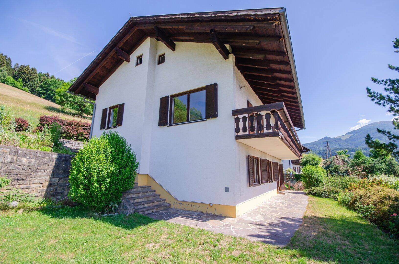 Charmantes Einfamilienhaus mit Balkon, umgeben von einem gepflegten Garten und Bergblick.