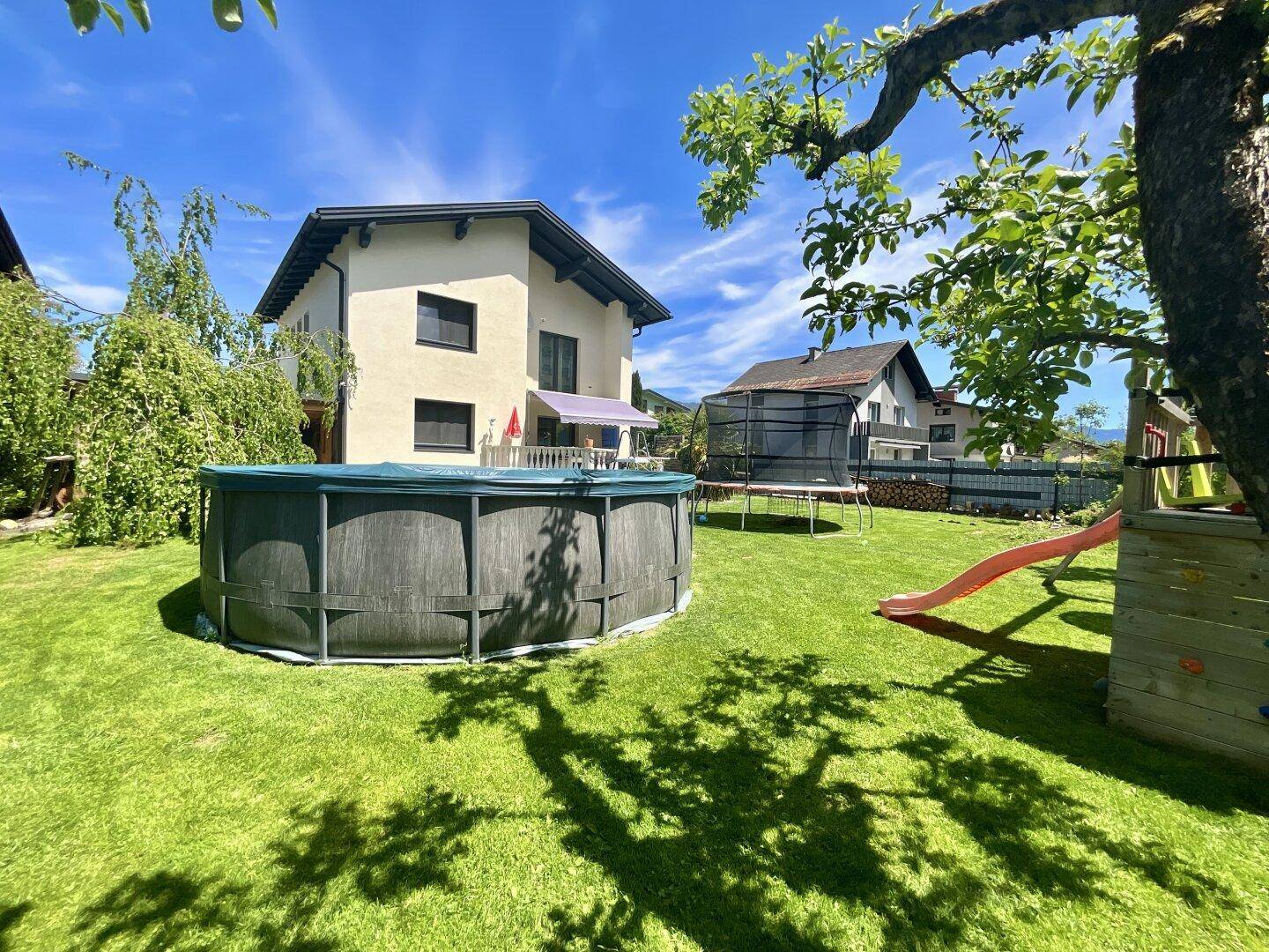 Gepflegter Garten mit Aufstellpool, Trampolin und Spielplatz für Kinder.