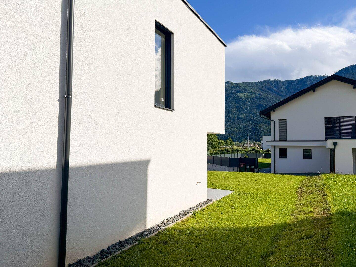 Seitenansicht des modernen Hauses mit Blick auf die umliegende Landschaft und Berge in der Ferne.