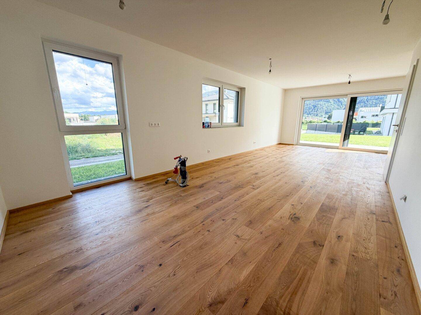 Geräumiger Wohnbereich mit Holzboden und großen Schiebetüren, die Zugang zum Garten bieten.