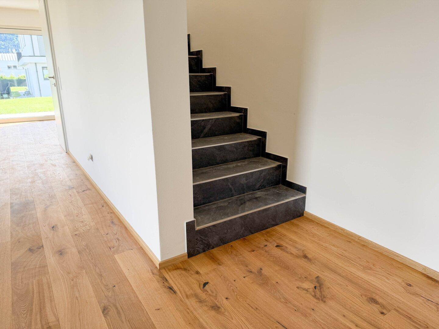 Treppenaufgang mit dunklen Stufen und hellem Holzboden im angrenzenden Bereich.