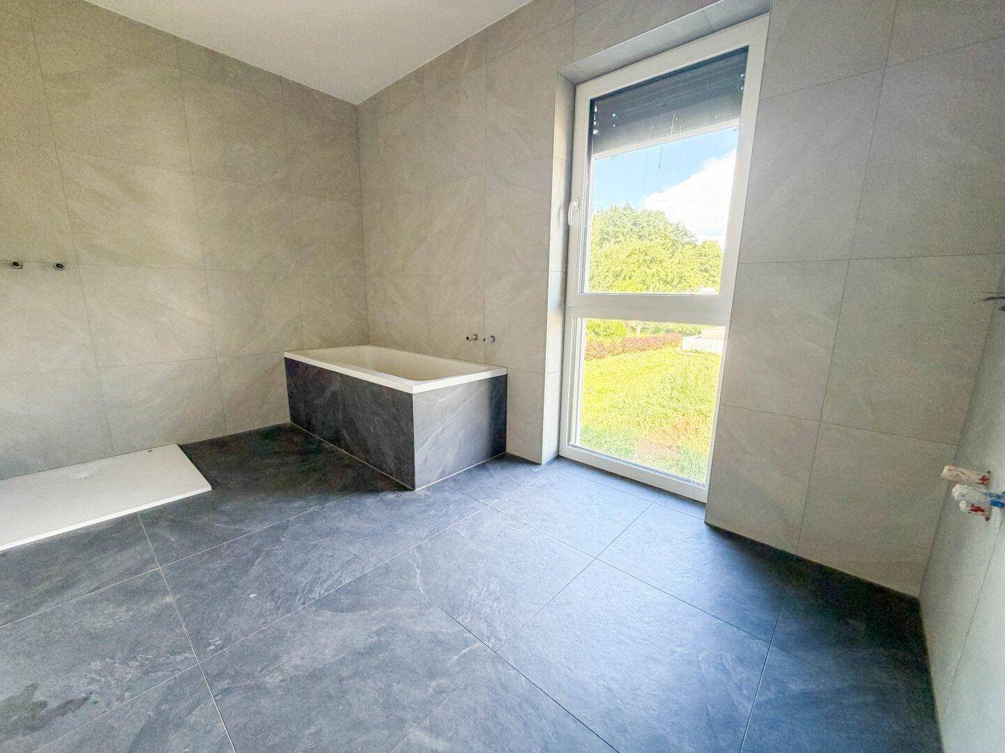 Modernes Badezimmer mit grauen Fliesen und einer eingebauten Badewanne, bereit für die Fertigstellung.