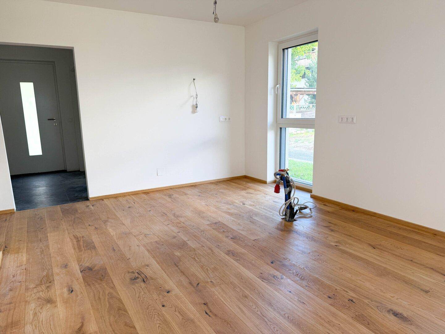 Geräumiger Wohnbereich mit Holzboden und einem Fenster, das viel natürliches Licht spendet.
