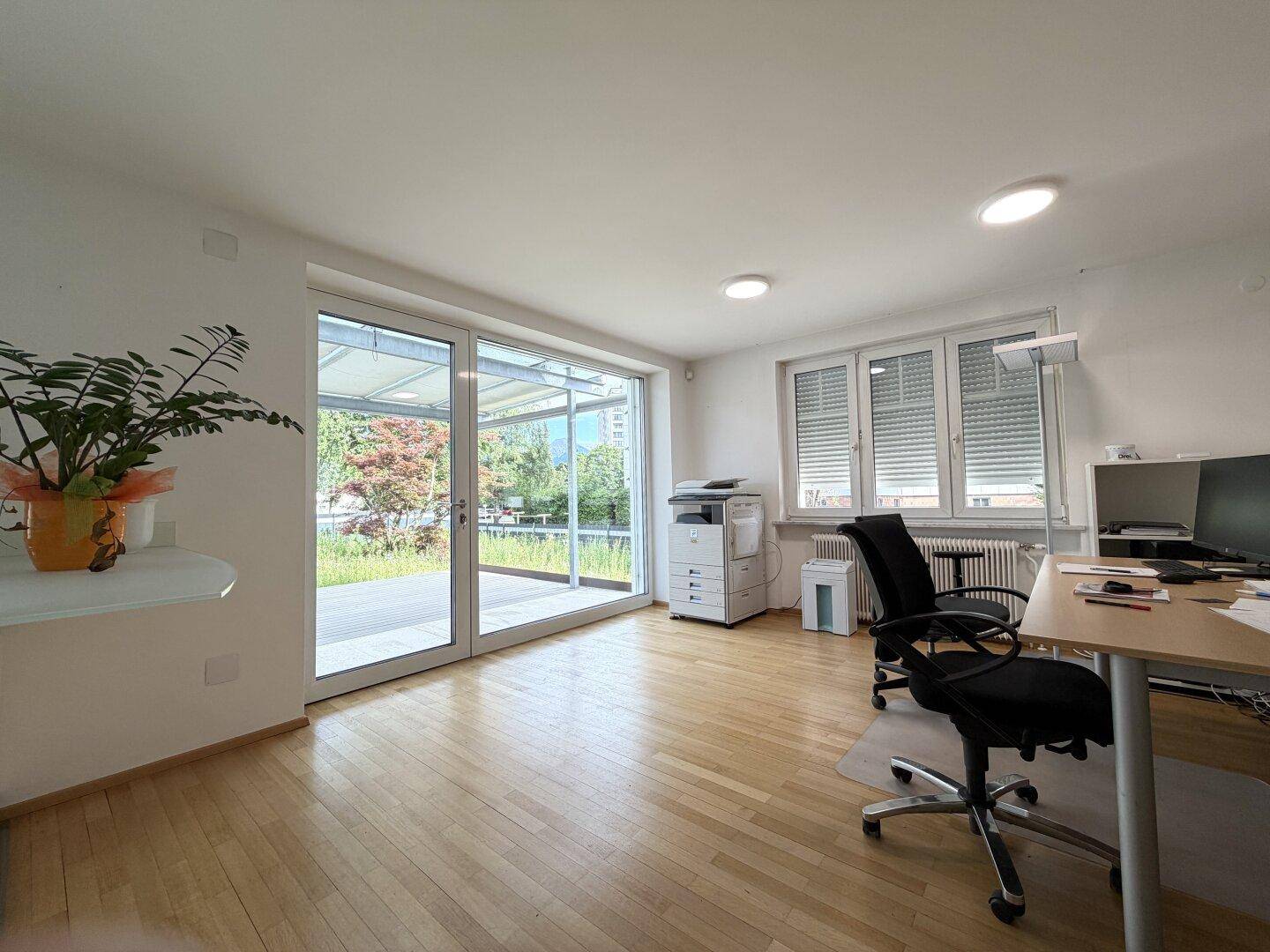 Helles Büro mit Holzparkett, großen Glasfronten und direktem Zugang zum Außenbereich.
