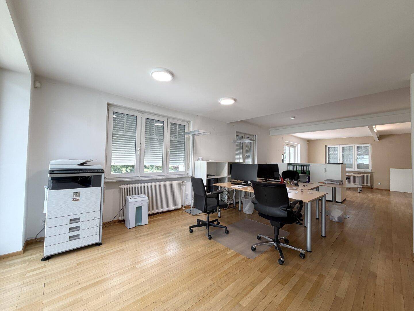 Geräumiges Büro mit offenem Grundriss, Holzparkett und mehreren Arbeitsplätzen.