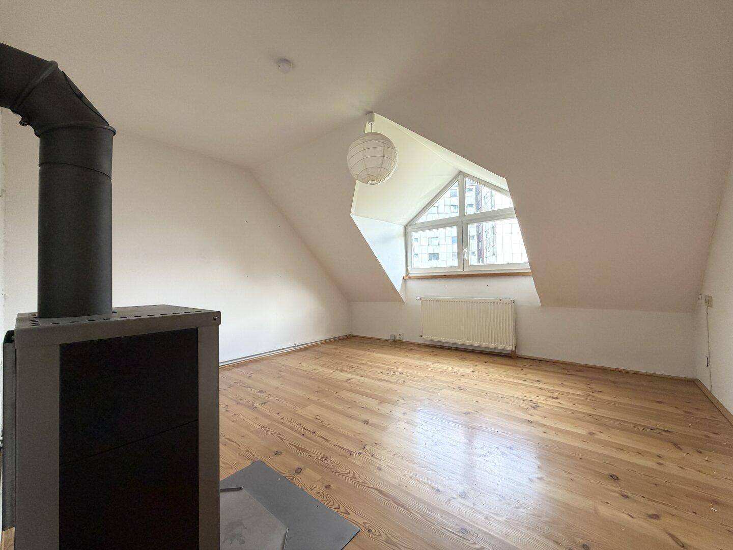 Dachzimmer mit Holzdielenboden, gemütlichem Holzofen und charakteristischem Giebelfenster.