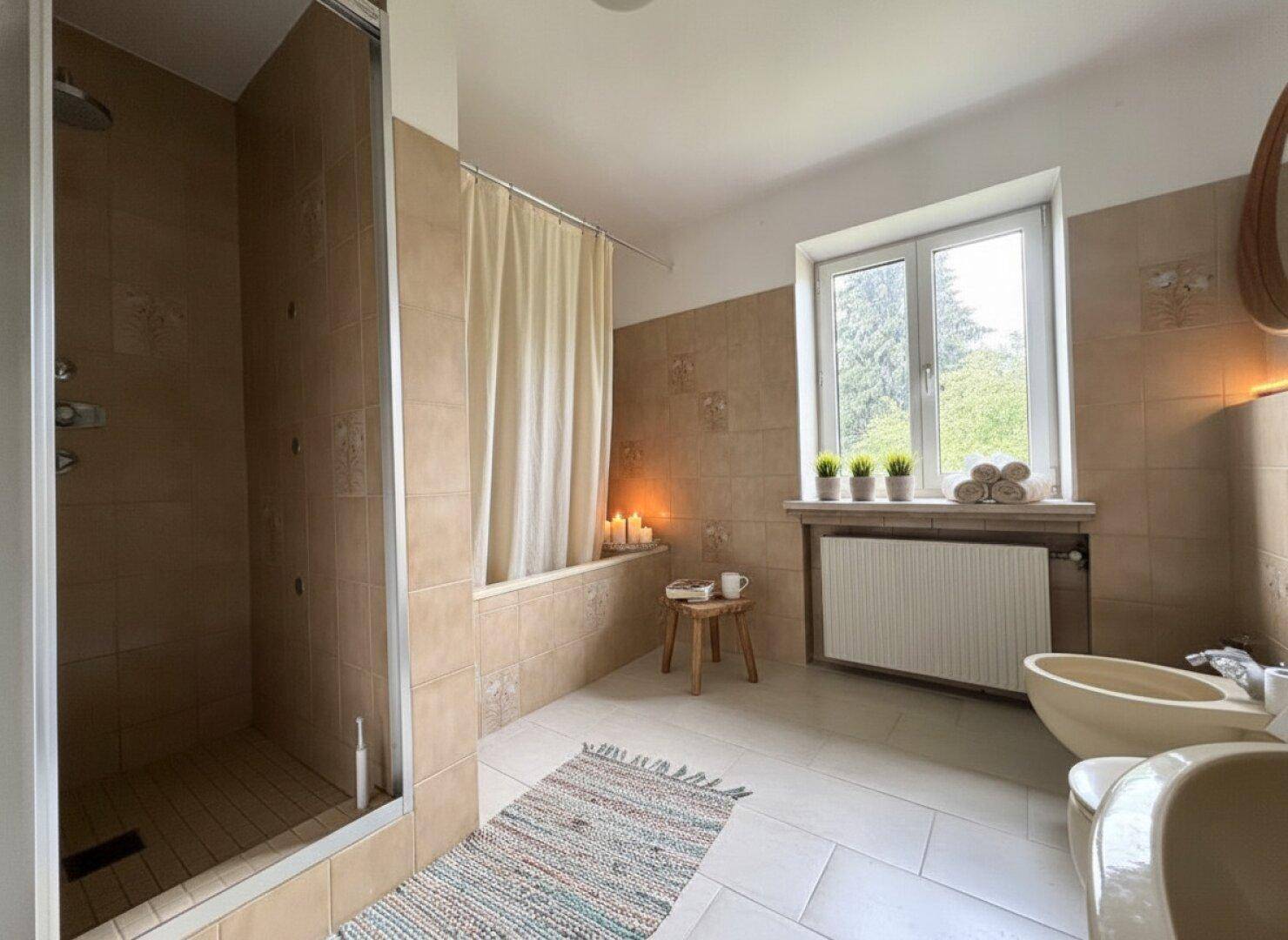 Geräumiges Badezimmer mit beigefarbenen Fliesen, einer Duschkabine und einem Fenster für natürliches Licht.