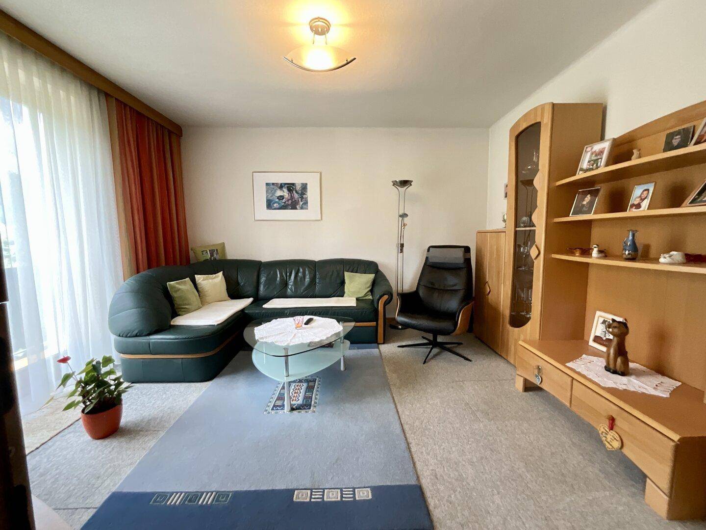 Gemütliches Wohnzimmer mit Ledersofa, Teppichboden und Holzmöbeln, ideal zum Entspannen.