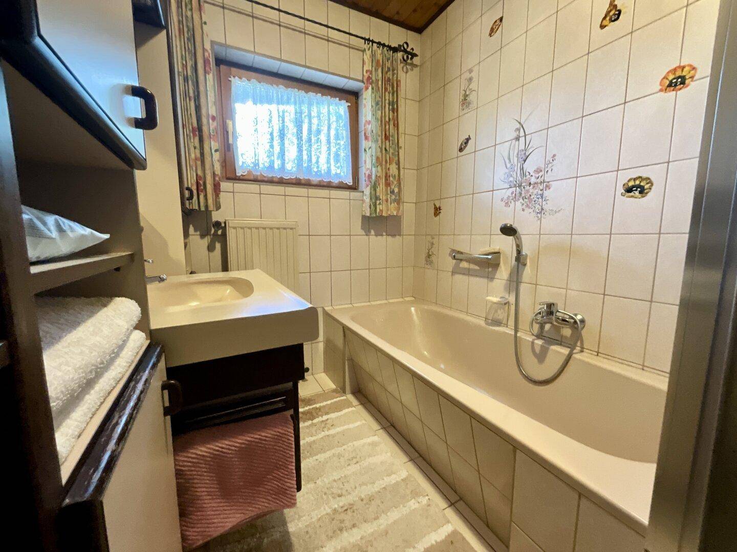 Badezimmer mit Badewanne, Waschbecken und Holzdecke, ausgestattet mit hellen Fliesen.