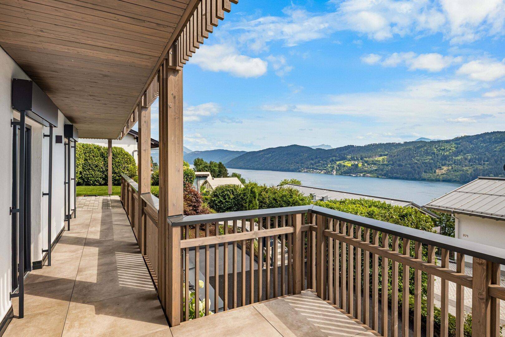Langer Balkon mit Holzgeländer und weitem Blick über den See und die bewaldeten Hügel.
