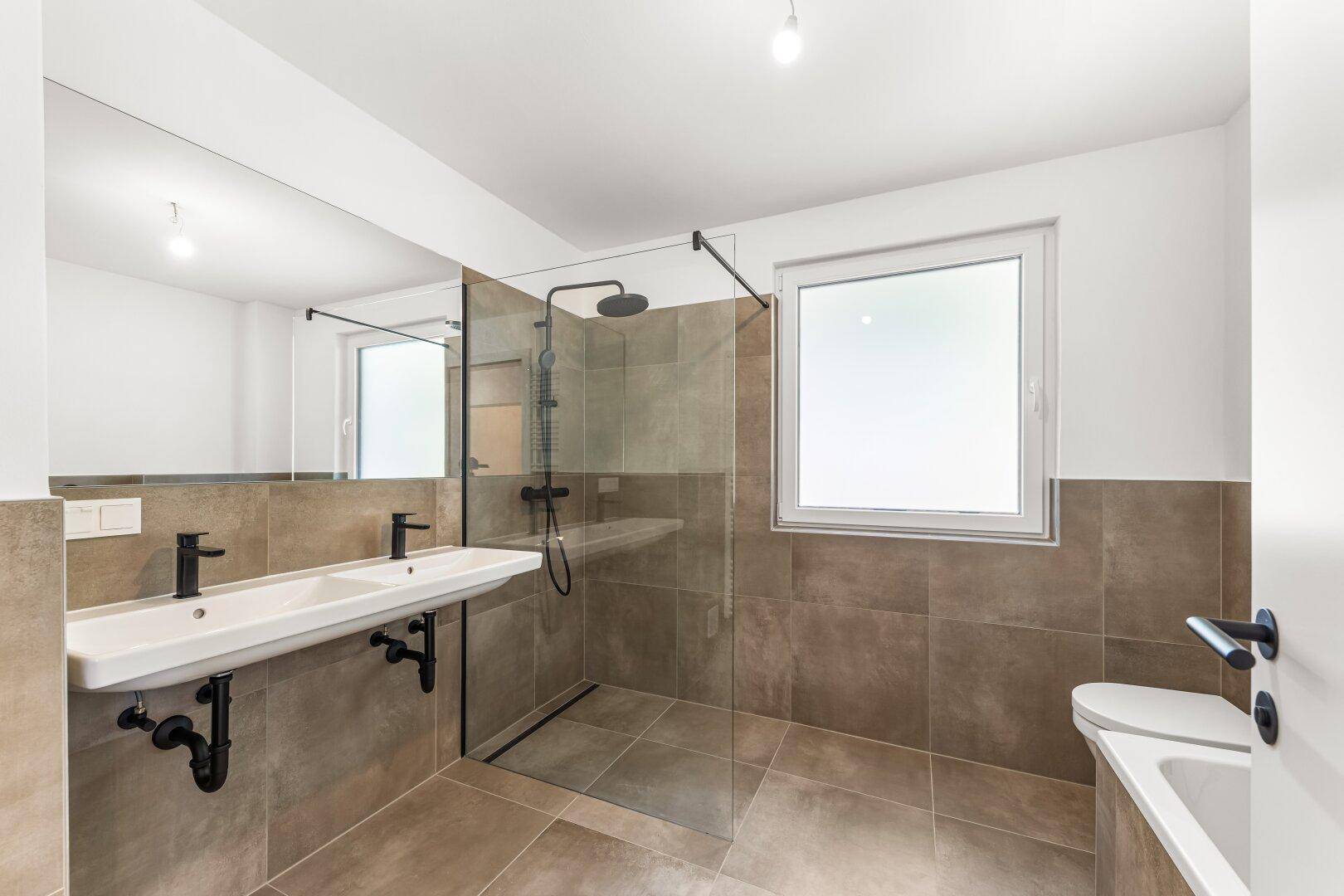 Modernes Badezimmer mit Doppelwaschbecken, großer Dusche und Fenster für Tageslicht.