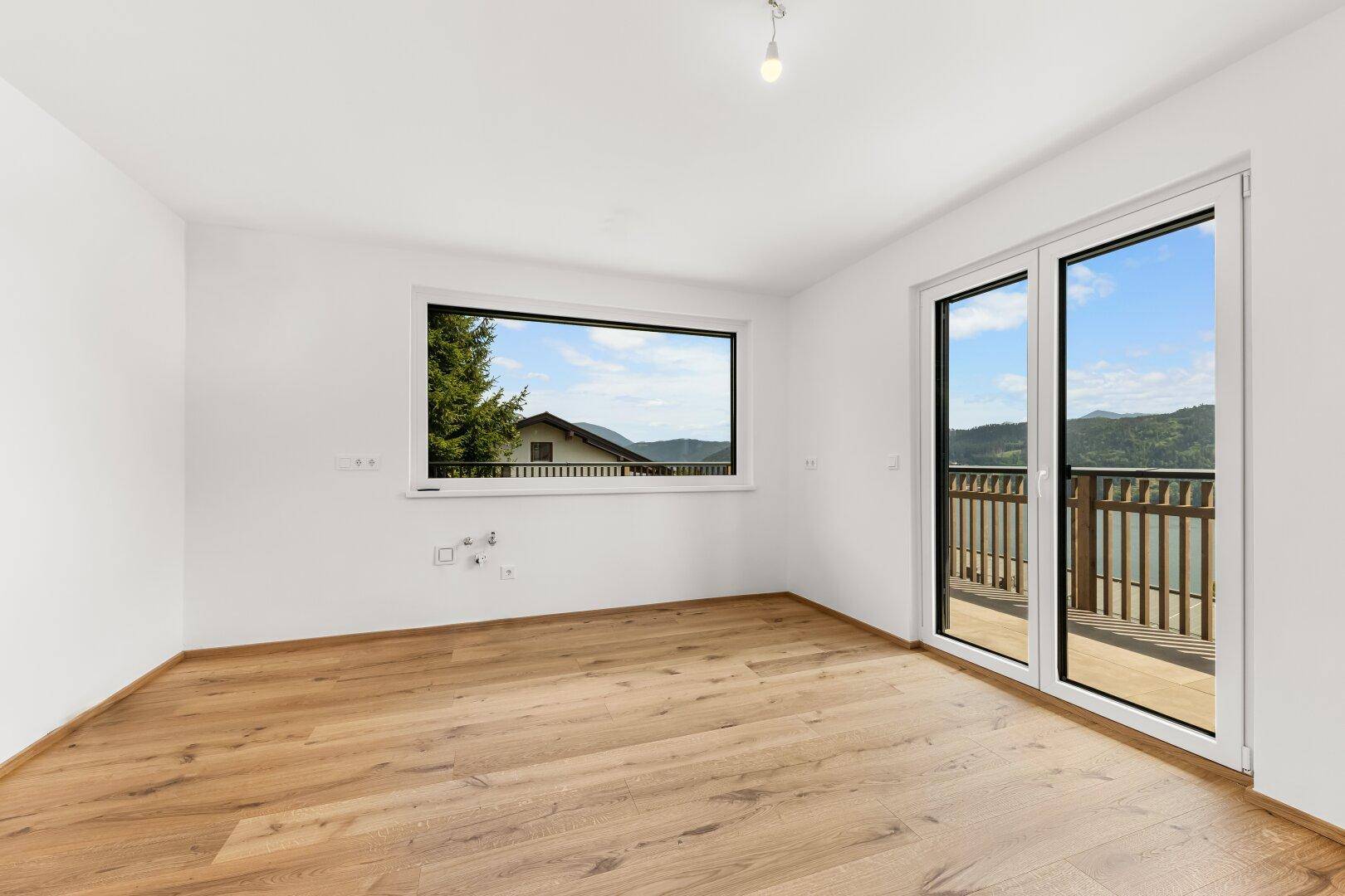 Helles Schlafzimmer mit Eichenparkett, großem Fenster und Balkonzugang mit Seeblick.