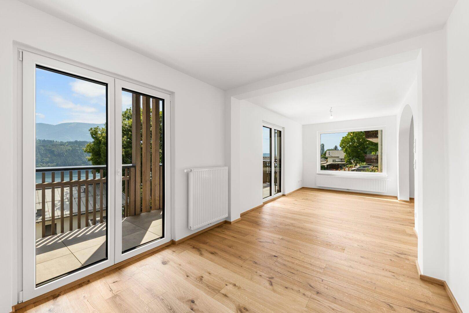 Geräumiger Wohn-Essbereich mit hellem Eichenparkett und Zugang zu einem Balkon mit Seeblick.