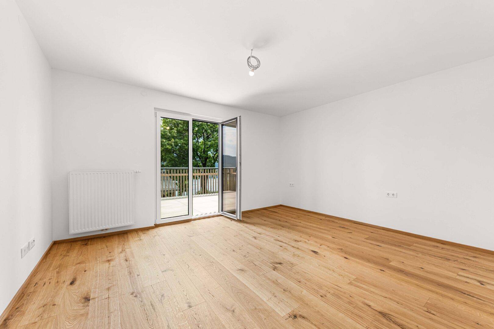 Geräumiges Schlafzimmer mit Eichenparkett und Balkonzugang, ideal für viel Tageslicht.