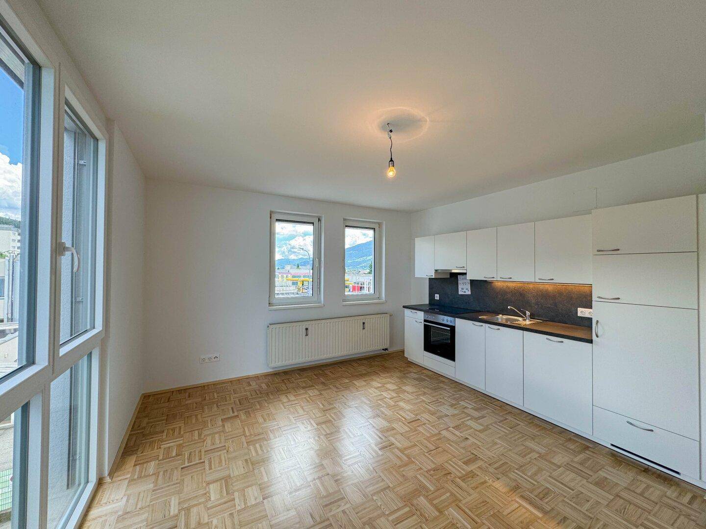Lichtdurchfluteter Wohnbereich mit moderner Küchenzeile, Parkettboden und weitem Ausblick.