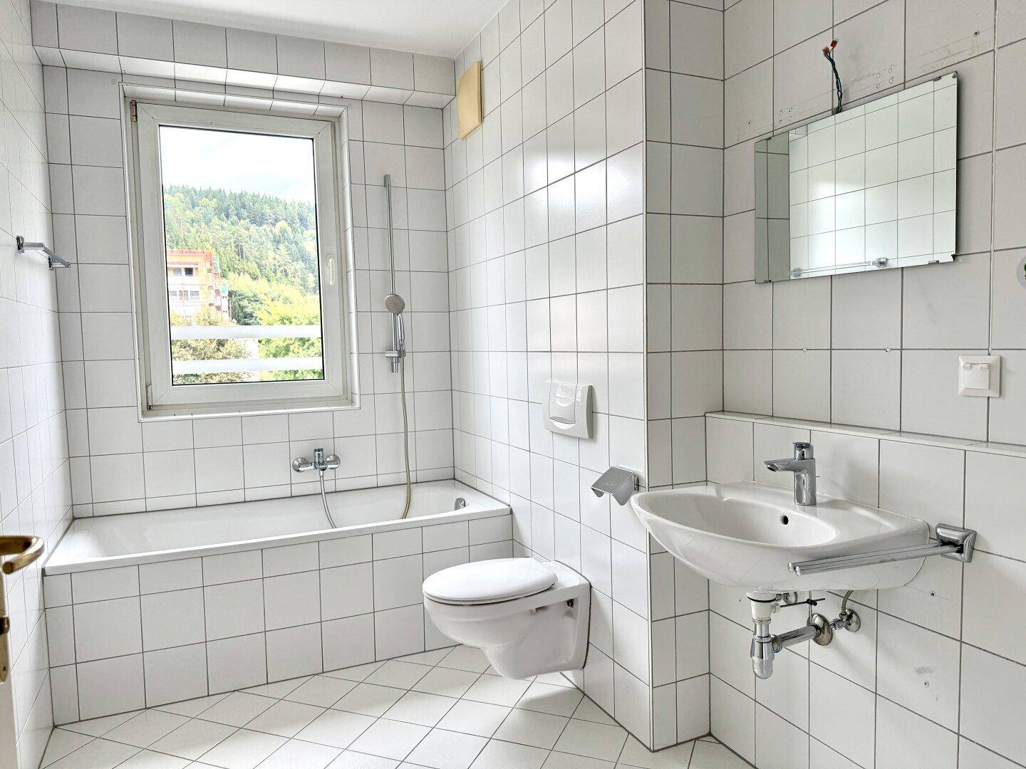 Gefliestes Badezimmer mit Badewanne, Toilette, Waschbecken und Fenster für Tageslicht.