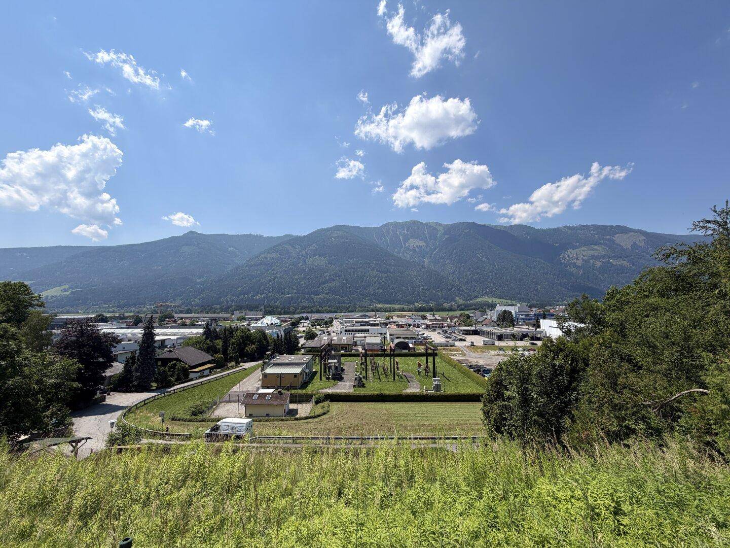 Weitblick über eine Stadt im Tal mit majestätischen Bergen im Hintergrund unter blauem Himmel.