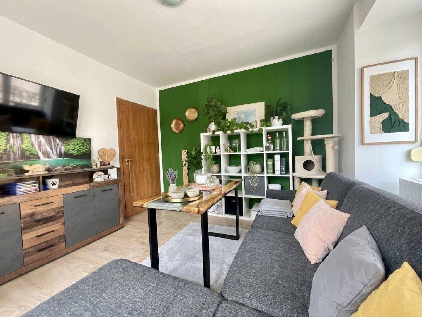 Gemütliches Wohnzimmer mit grüner Akzentwand, Sofa und vielen Pflanzen.