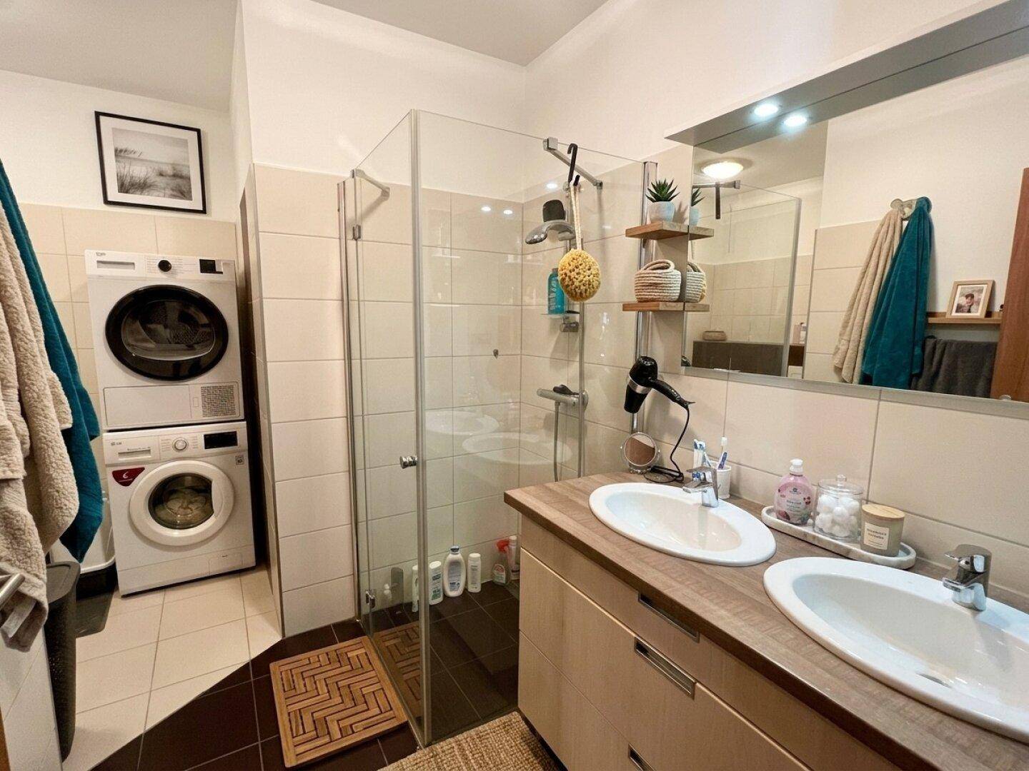 Modernes Badezimmer mit Doppelwaschbecken, Dusche und integrierter Waschmaschine.