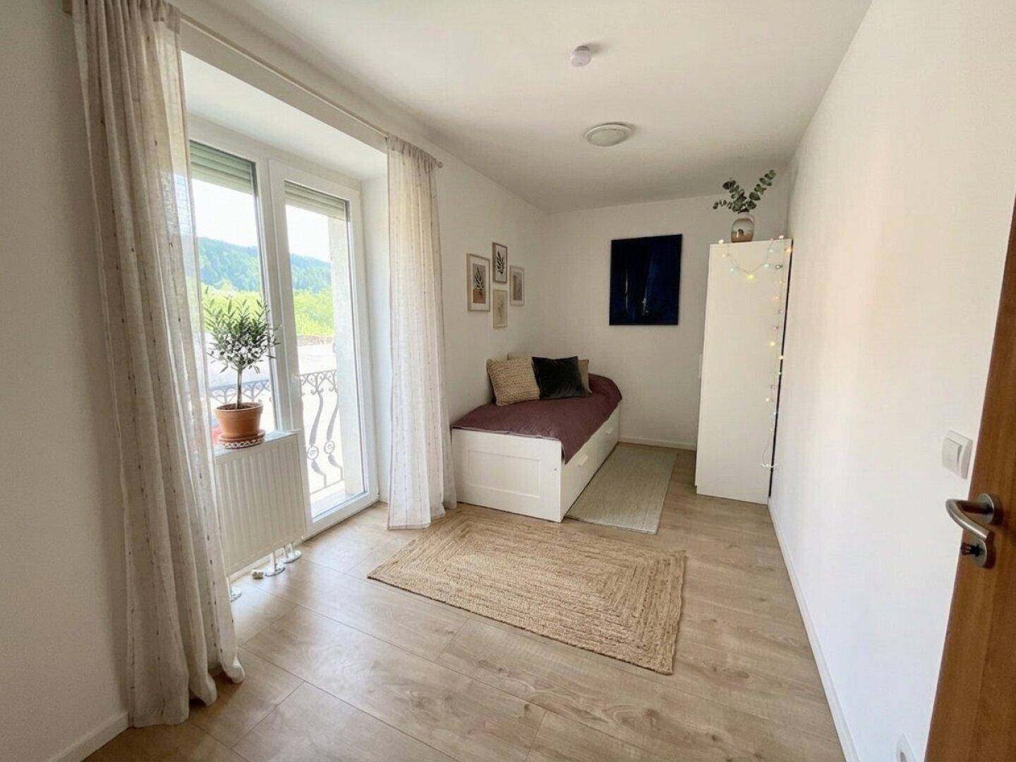Schlafzimmer mit Balkonzugang, Holzboden und minimalistischer Einrichtung.