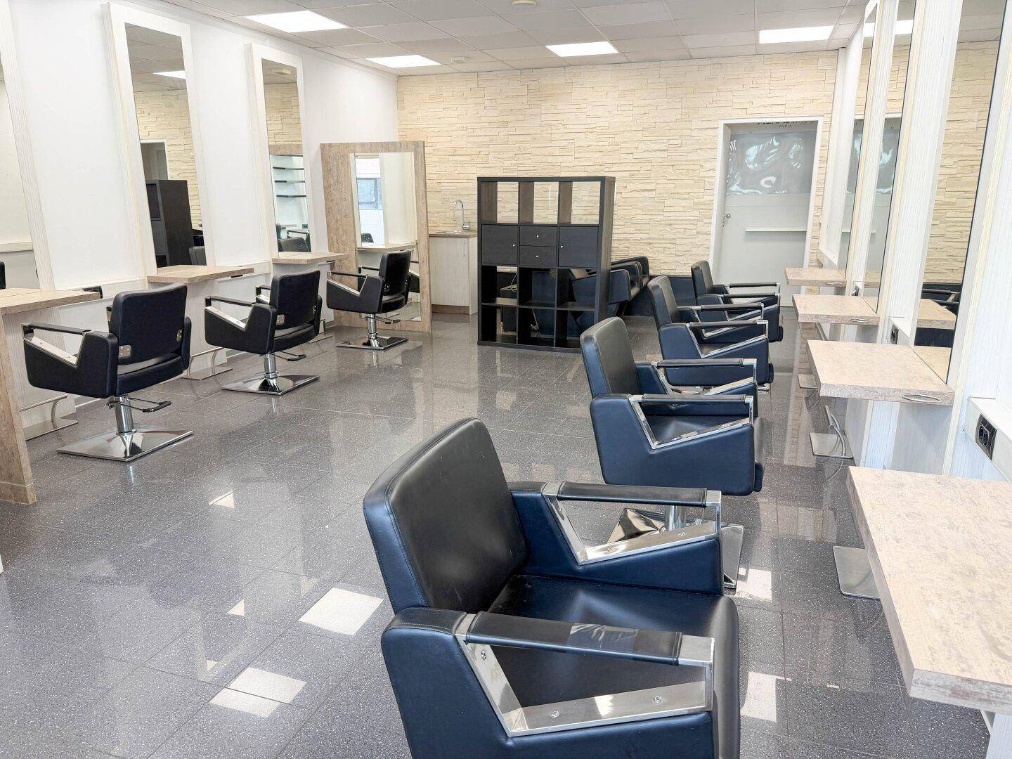 Heller Friseursalon mit modernen Styling-Stühlen, großen Spiegeln und einer dekorativen Steinwand.