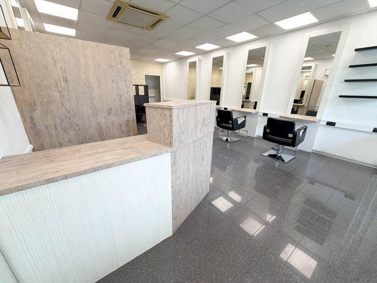 Empfangsbereich eines Friseursalons mit moderner Theke und Blick auf die Styling-Stationen im Hintergrund.