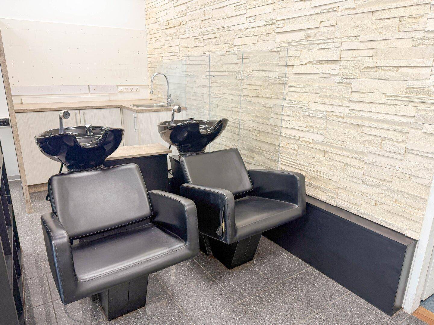 Waschbereich im Friseursalon mit zwei modernen Waschbecken und einer dekorativen Steinwand.