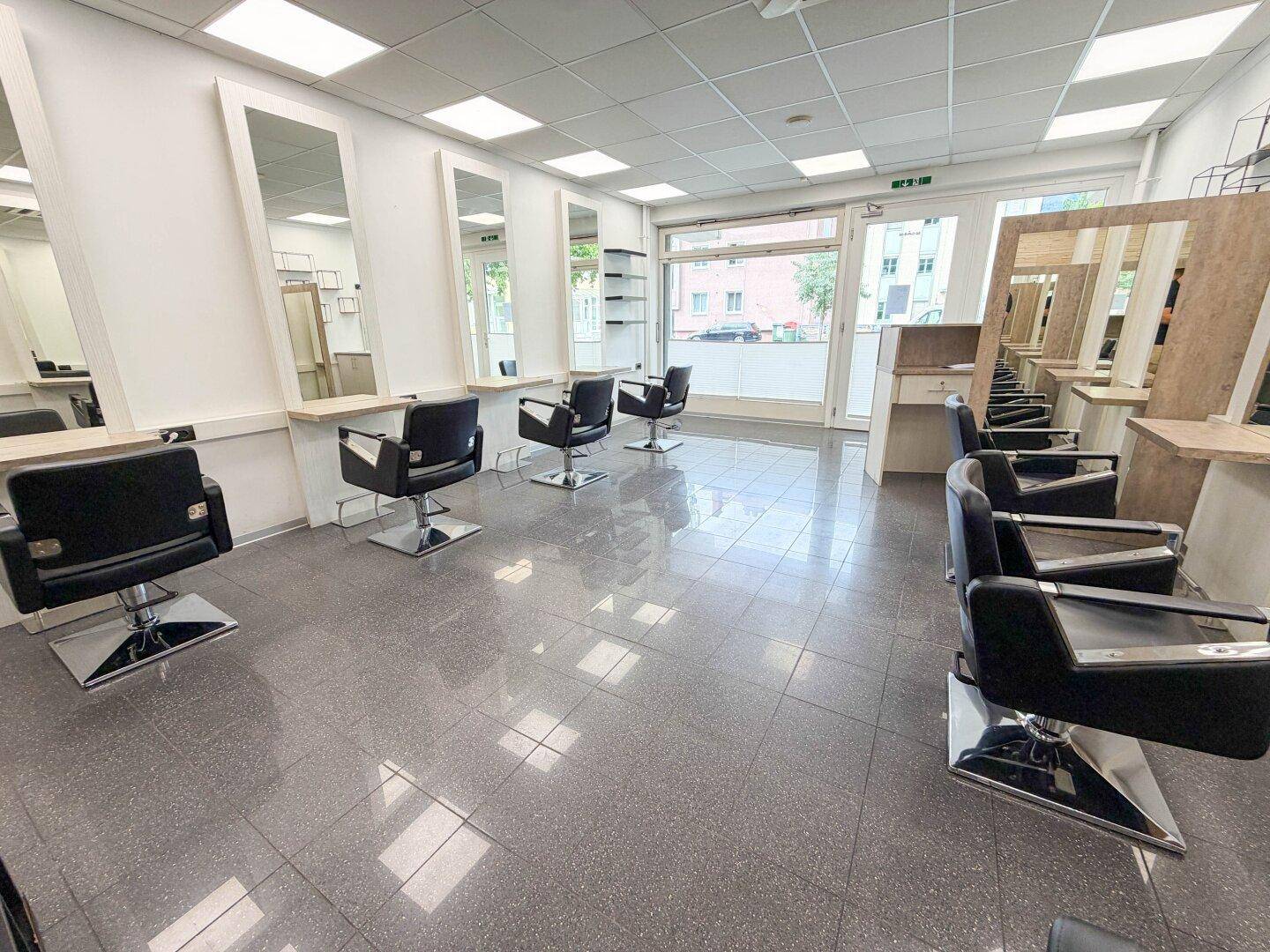 Geräumiger und heller Friseursalon mit zahlreichen Styling-Plätzen und großen Fenstern zur Straße.