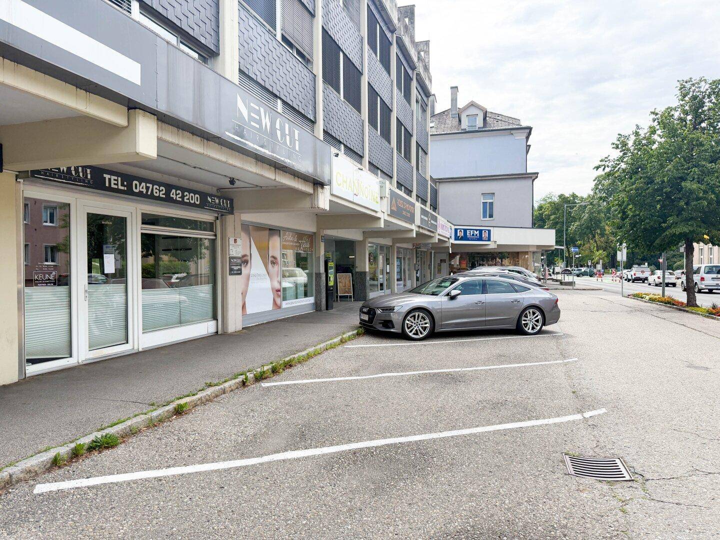 Ansicht der Geschäftsfassade mit Schaufenstern und angrenzenden Parkmöglichkeiten an einer belebten Straße.