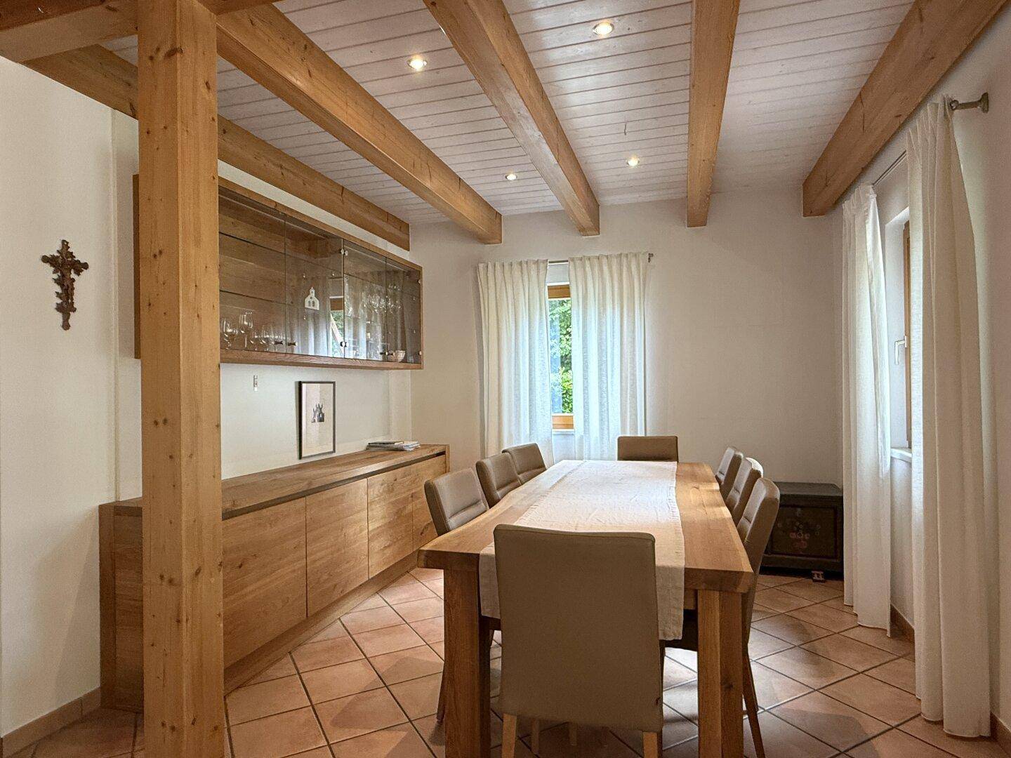 Gemütlicher Essbereich mit großem Holztisch, Holzbalken und passenden Einbaumöbeln.