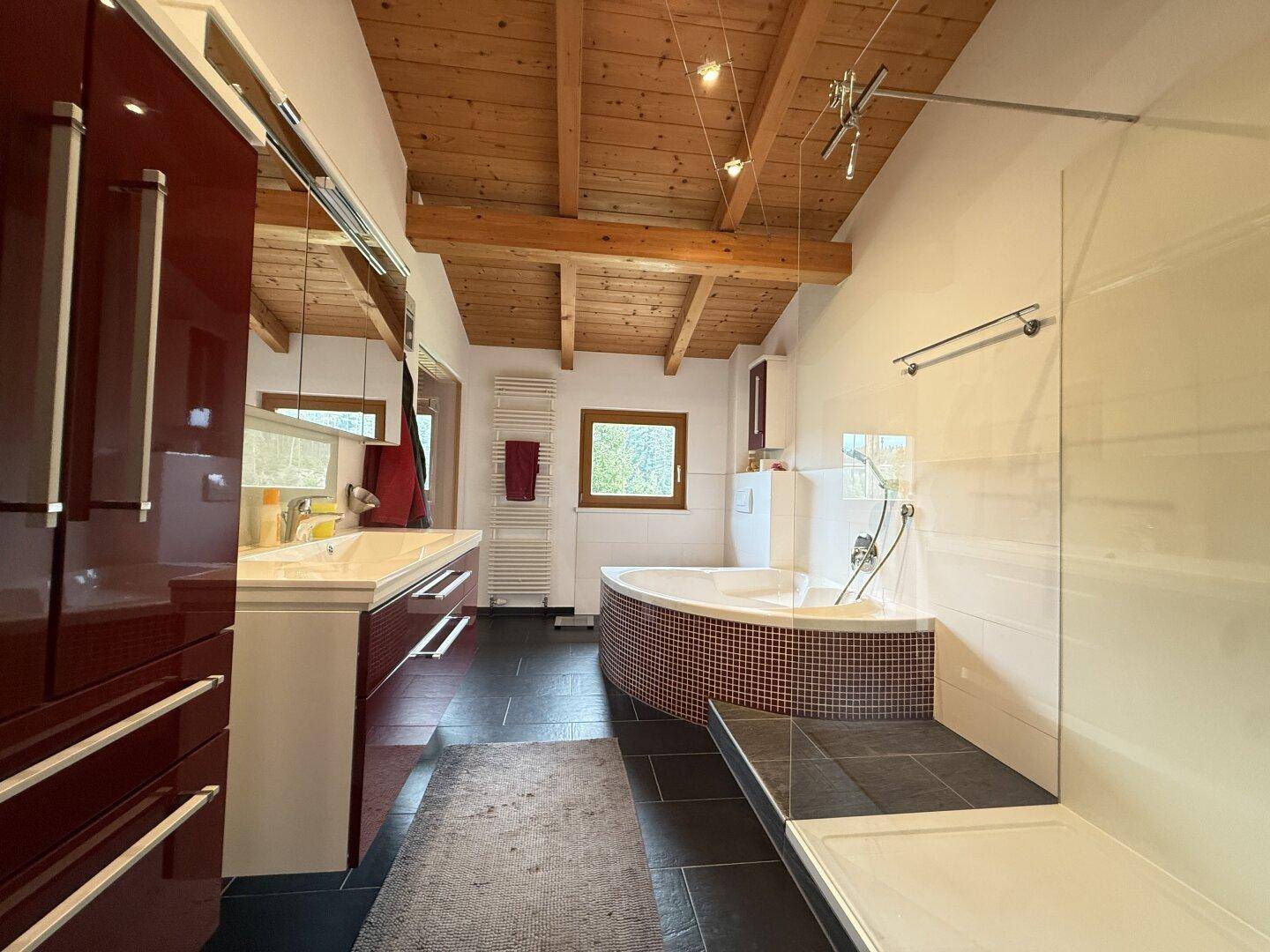 Modernes Badezimmer mit Eckbadewanne, Dusche, Doppelwaschbecken und Holzbalkendecke.