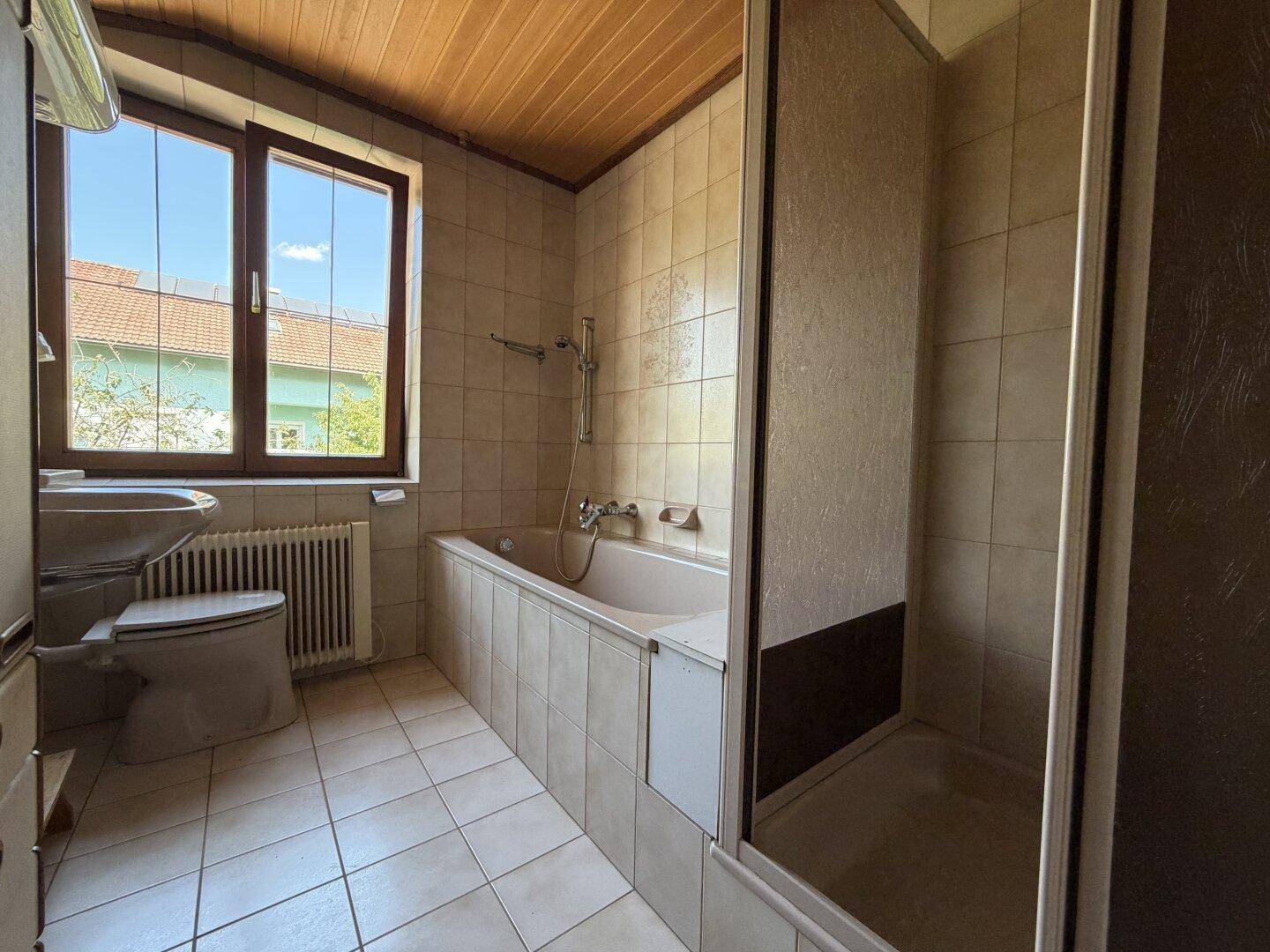 Badezimmer mit Fliesenboden, Badewanne, Duschkabine und Fenster für Tageslicht.