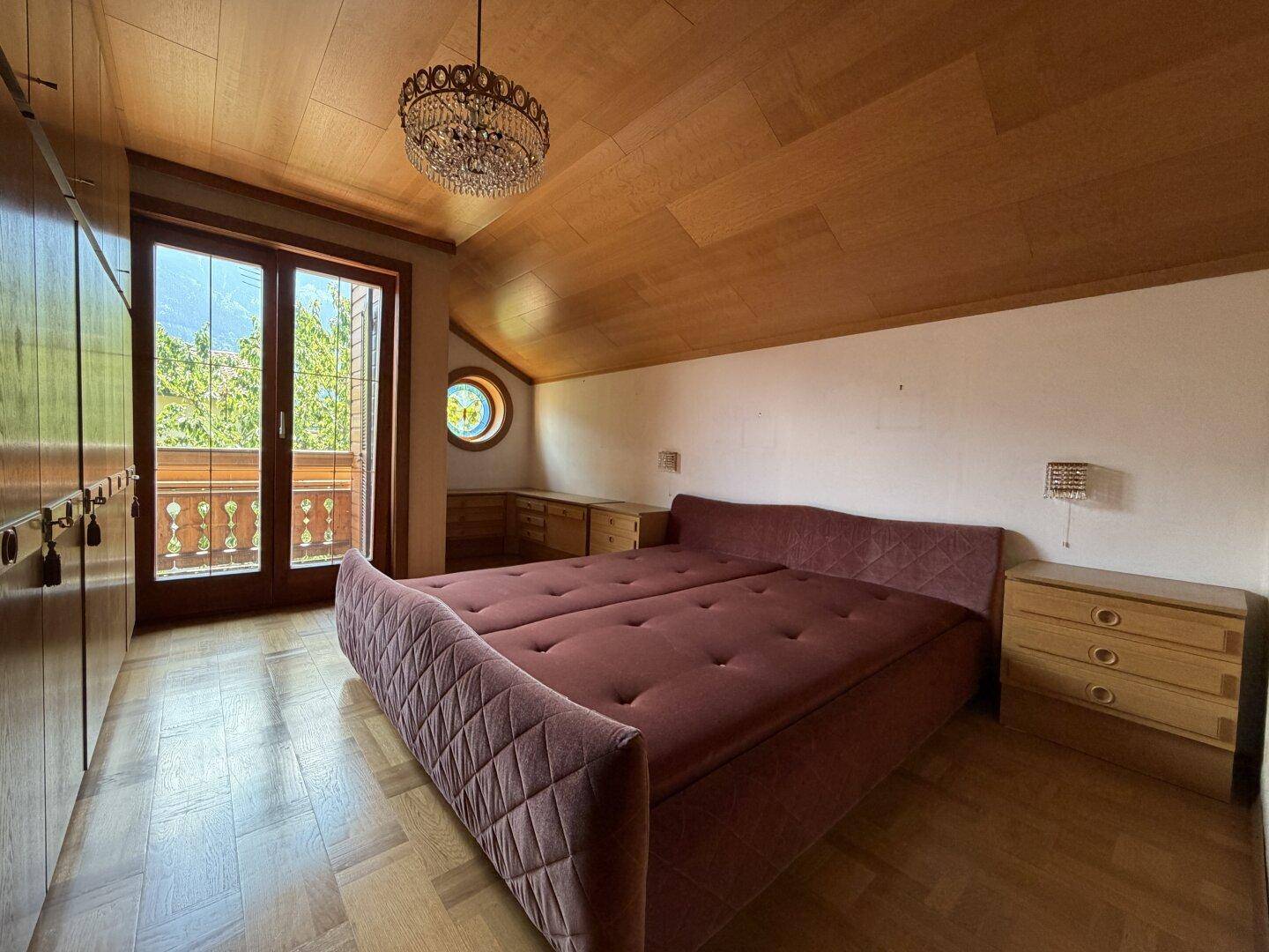 Gemütliches Schlafzimmer mit Holzdecke, Dachschräge und Zugang zu einem Balkon.
