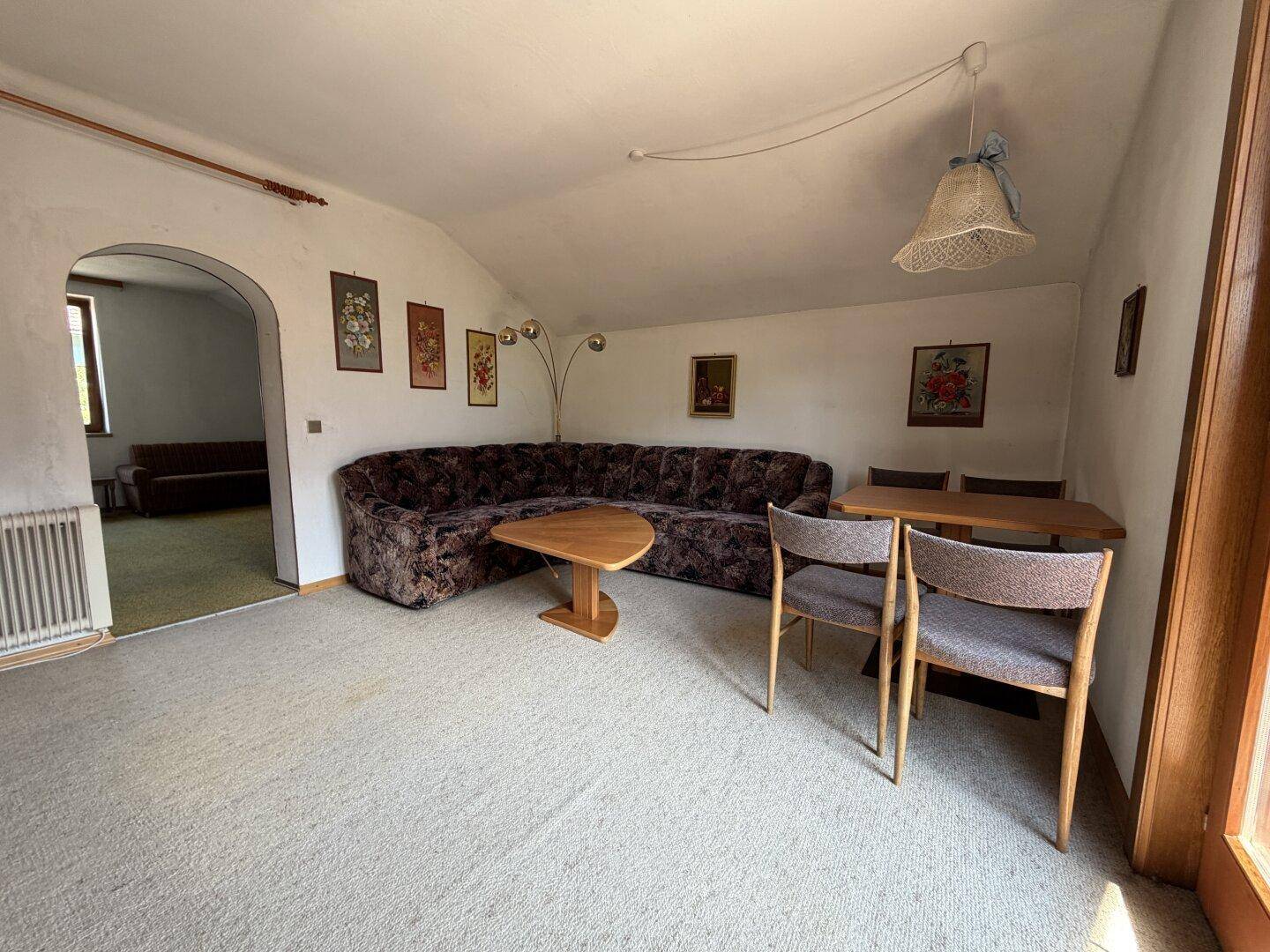 Wohnzimmer mit Teppichboden, großer Eckcouch und Durchgang zu einem weiteren Raum.