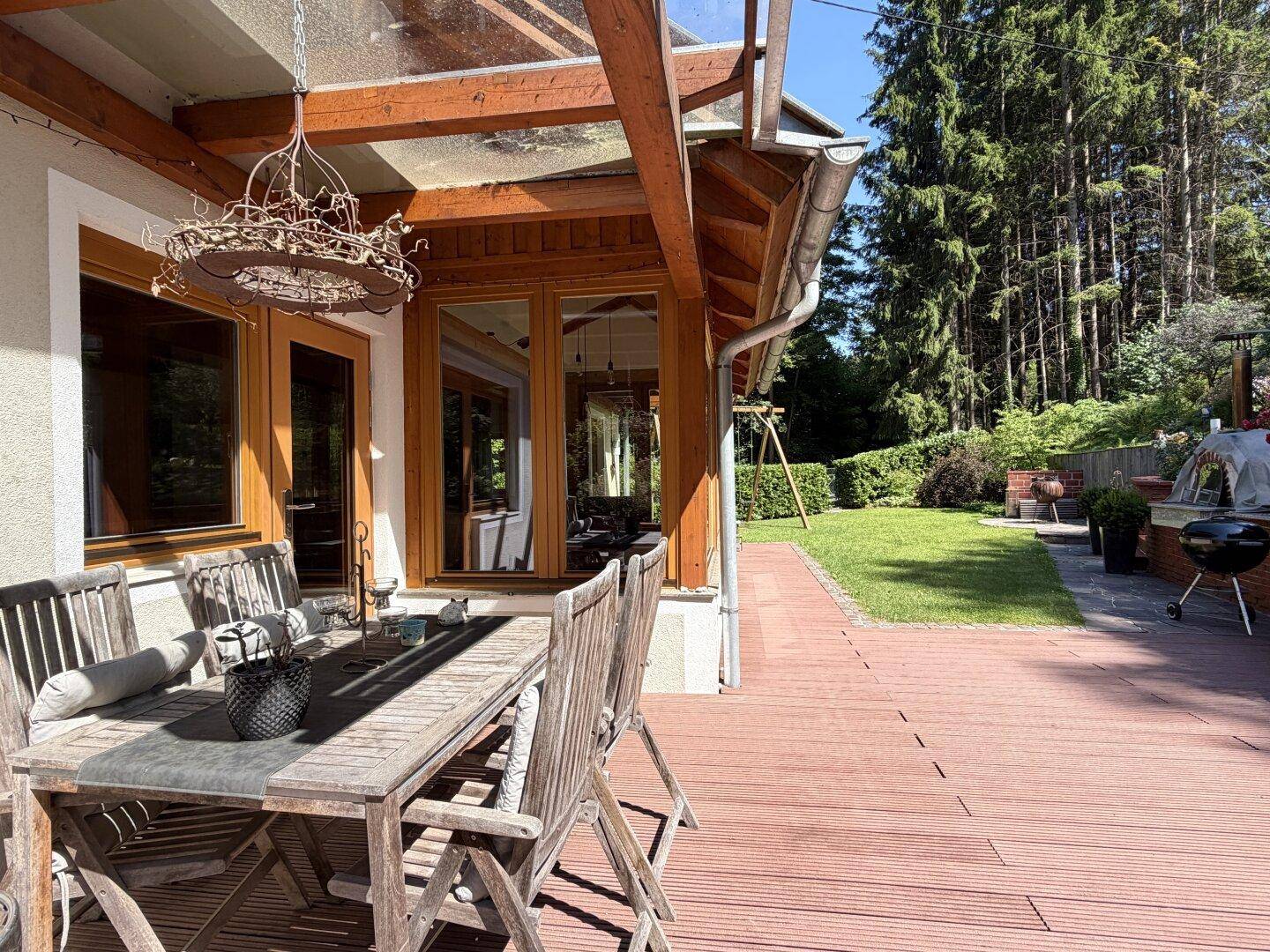 Überdachte Holzterrasse mit Esstisch und Stühlen, direktem Zugang zum Garten und Waldblick.