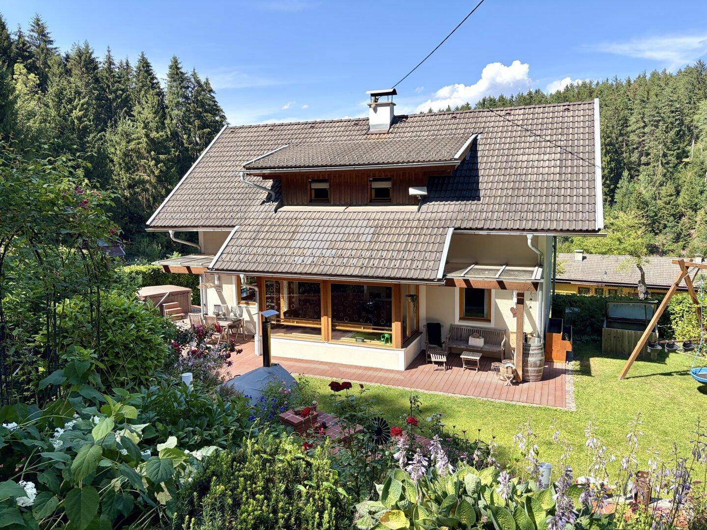 Das Haus von außen mit gepflegtem Garten, umgeben von Bäumen und grüner Landschaft.