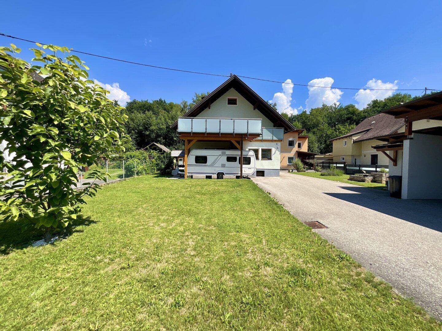 Weitläufige Rasenfläche vor dem Haus mit Zufahrt und geparktem Wohnwagen.