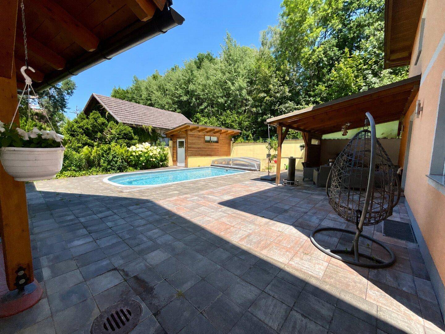 Großzügiger Außenbereich mit Pool, gepflasterter Terrasse und überdachtem Sitzbereich.