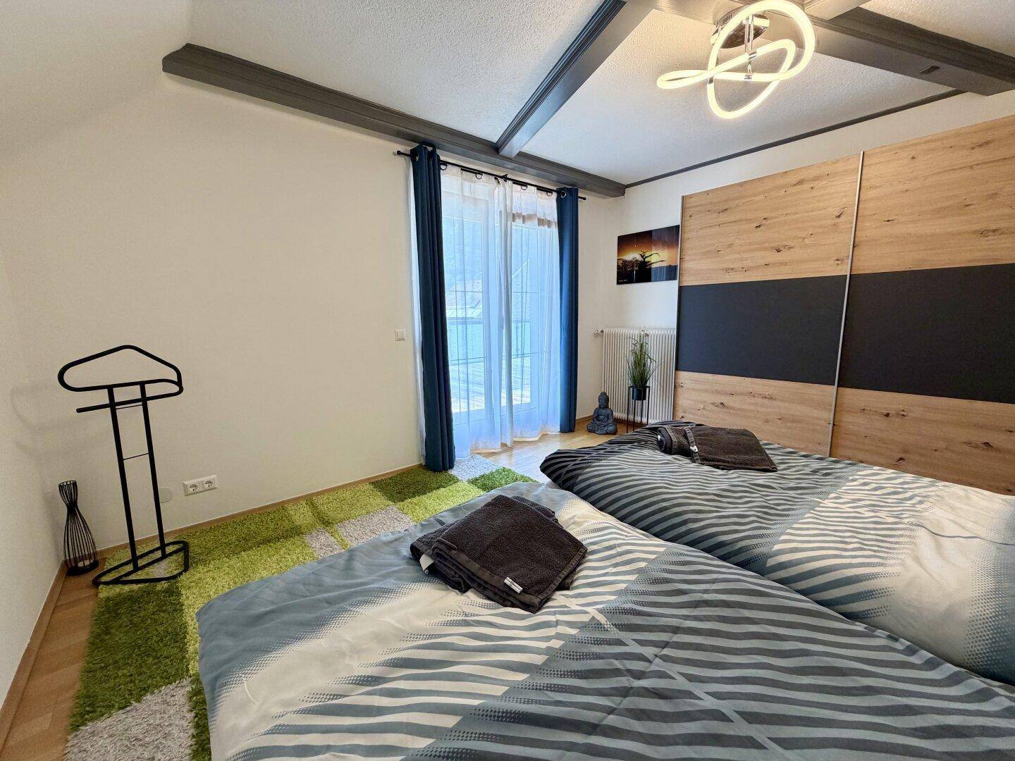Gemütliches Schlafzimmer mit zwei Betten, Kleiderschrank und sichtbaren Deckenbalken.