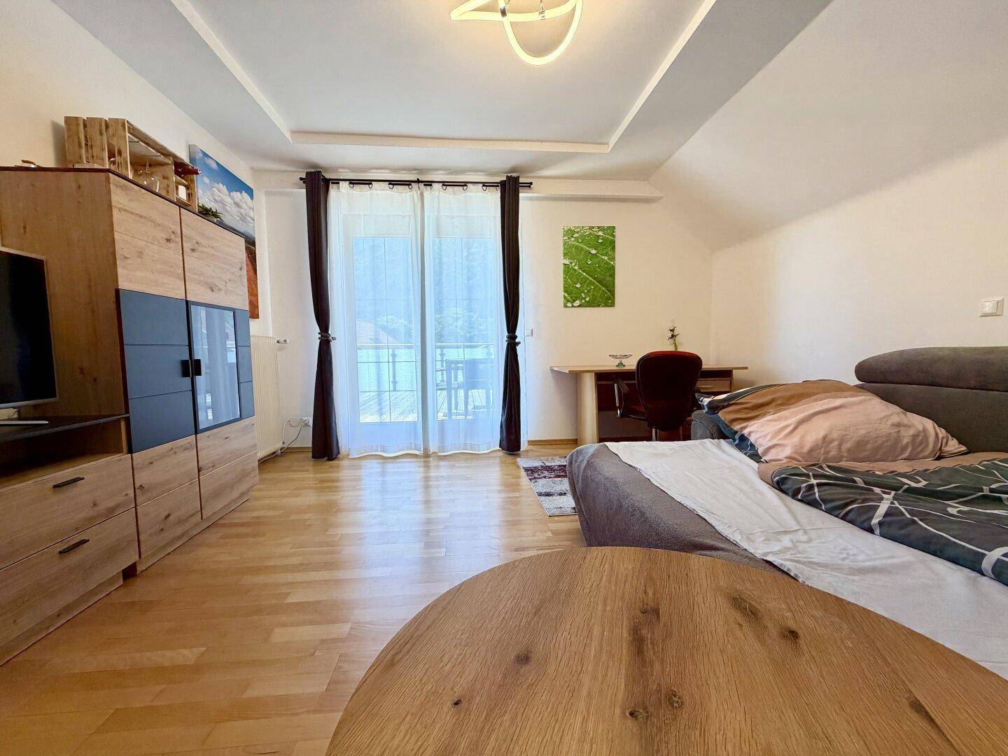 Helles Wohnzimmer mit Holzboden, TV-Möbel und Zugang zu einem Balkon.