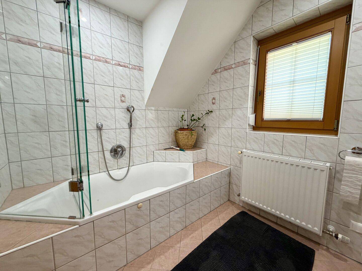 Gefliestes Badezimmer mit Badewanne, Fenster und Dachschräge.