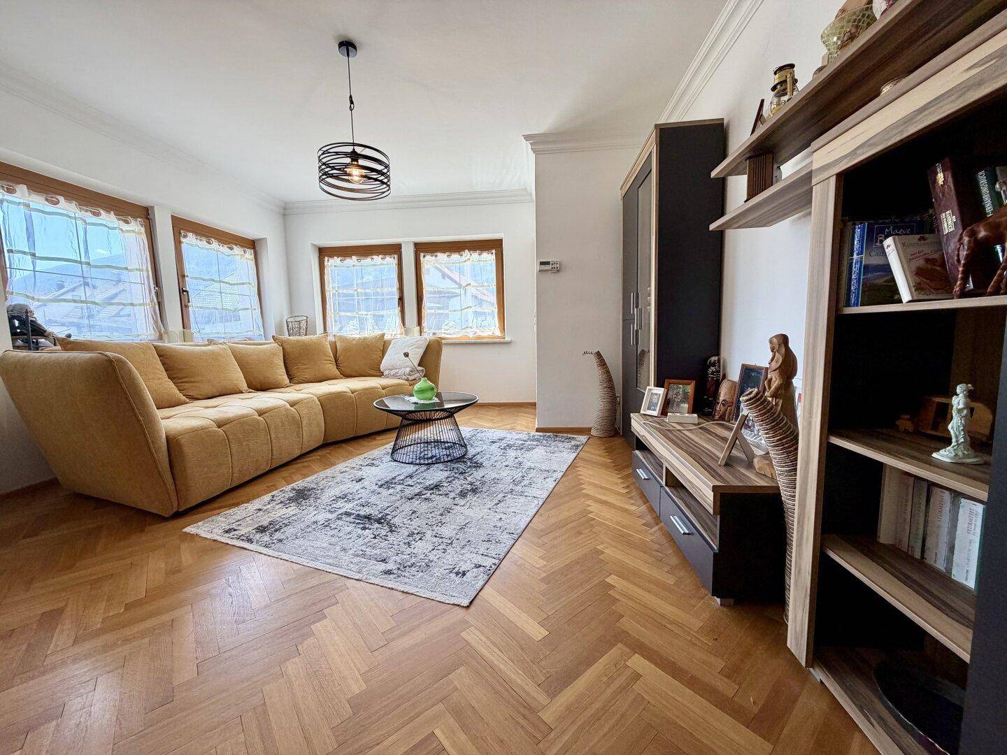 Geräumiges Wohnzimmer mit gelbem Ecksofa, Fischgrätparkett und modernen Möbeln.