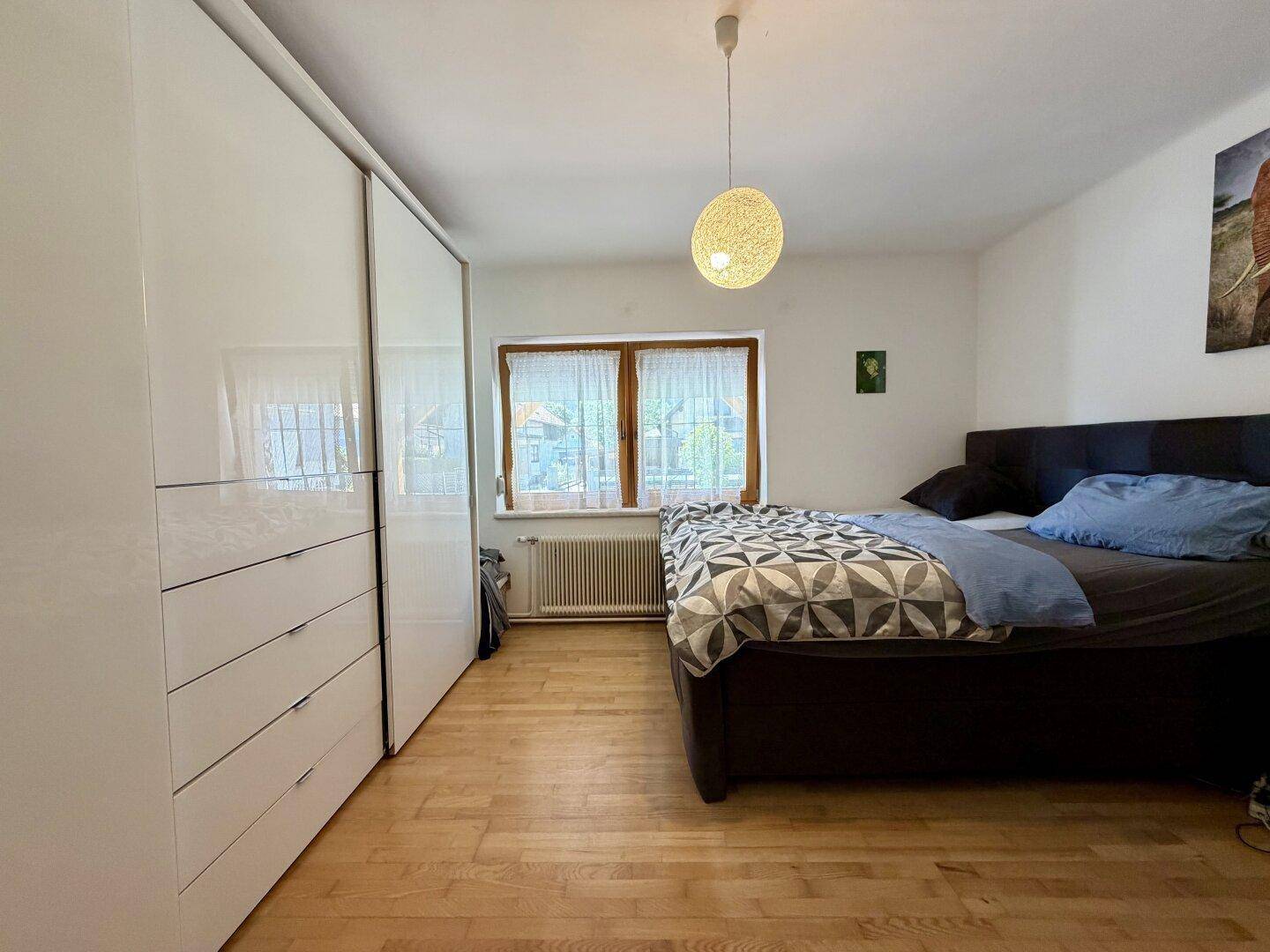 Helles Schlafzimmer mit Doppelbett, großem weißen Kleiderschrank und Holzboden.