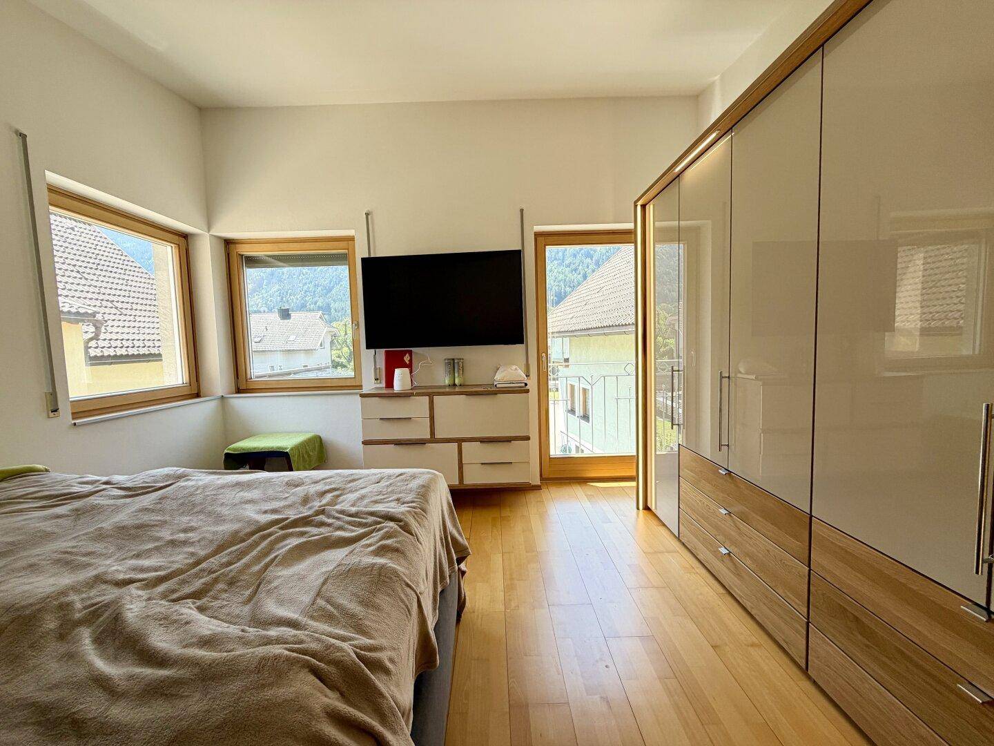 Helles Schlafzimmer mit Doppelbett, Kleiderschrank und Zugang zu einem französischen Balkon.