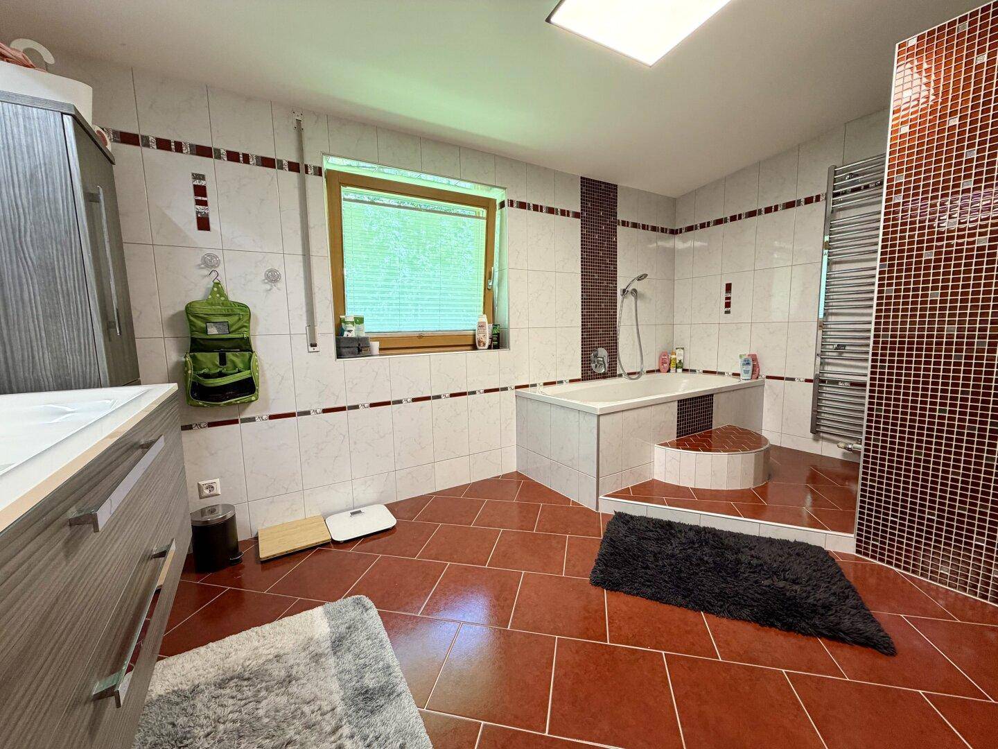 Geräumiges Badezimmer mit Badewanne, roten und weißen Fliesen und Fenster.