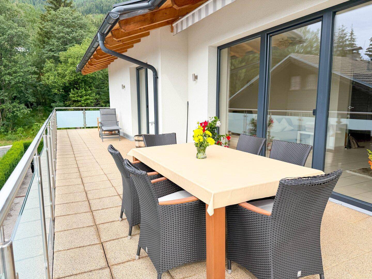 Helle Terrasse mit Esstisch und Zugang zum Innenbereich, umgeben von Natur.